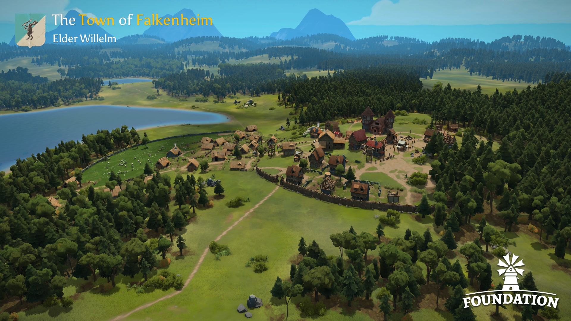 An expansive, high-angle view of the growing town of Falkenheim from the game "Foundation." The town, featuring numerous buildings and a stone wall, sprawls across a green landscape beside a large lake. Surrounding the settlement are extensive forests and distant mountains under a clear sky.