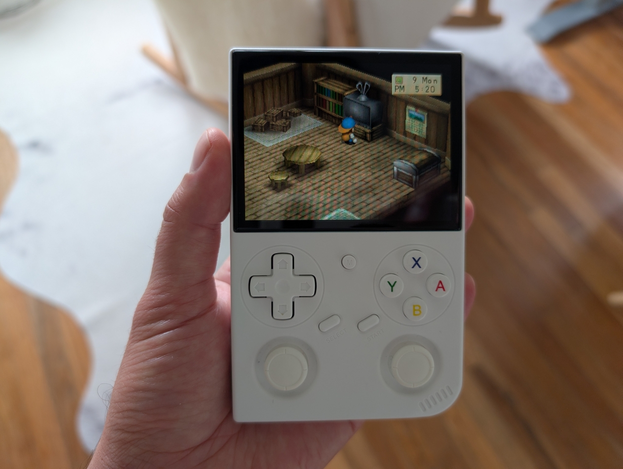 A hand holding Anbernic RG35XX Pro, with a boy protagonist from Harvest Moon: Back to Nature. Photo by the author.