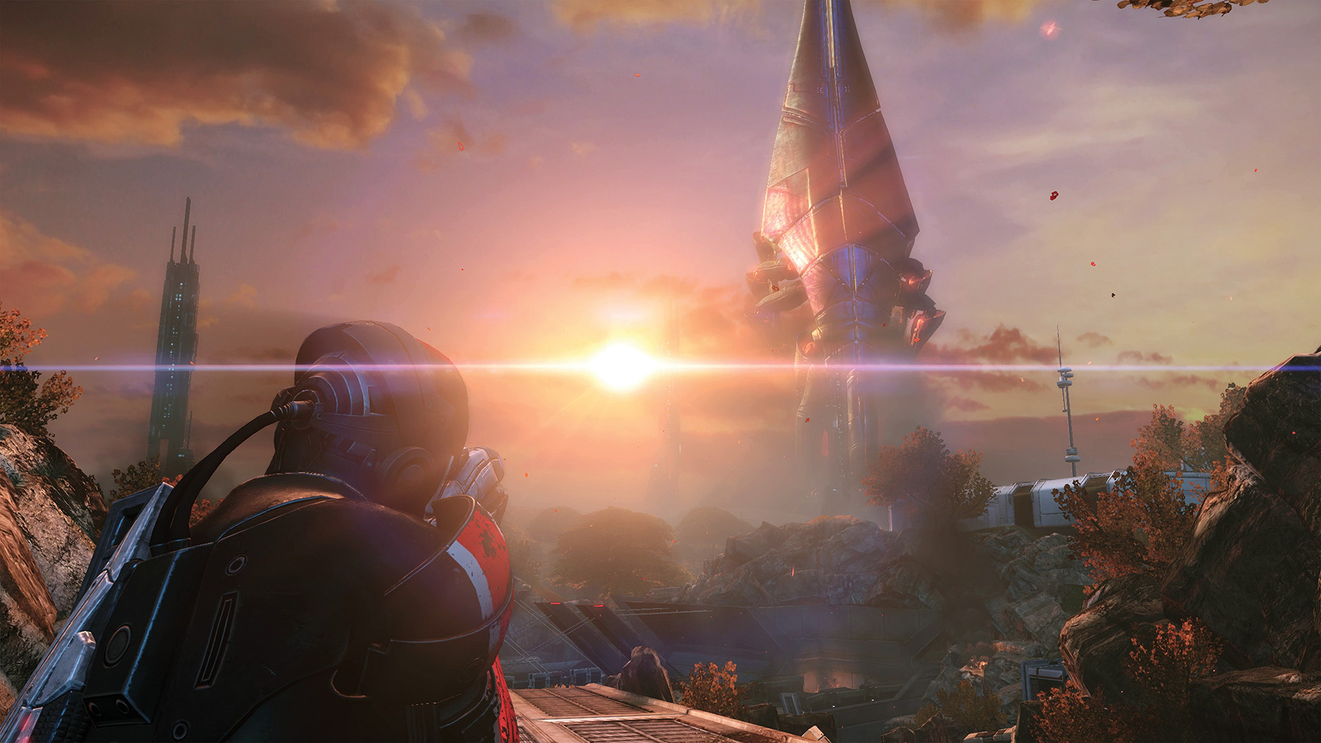 A screenshot from Mass Effect, shows a character in futuristic armor aiming a weapon towards a bright light in the distance, with a large alien structure towering in the background.