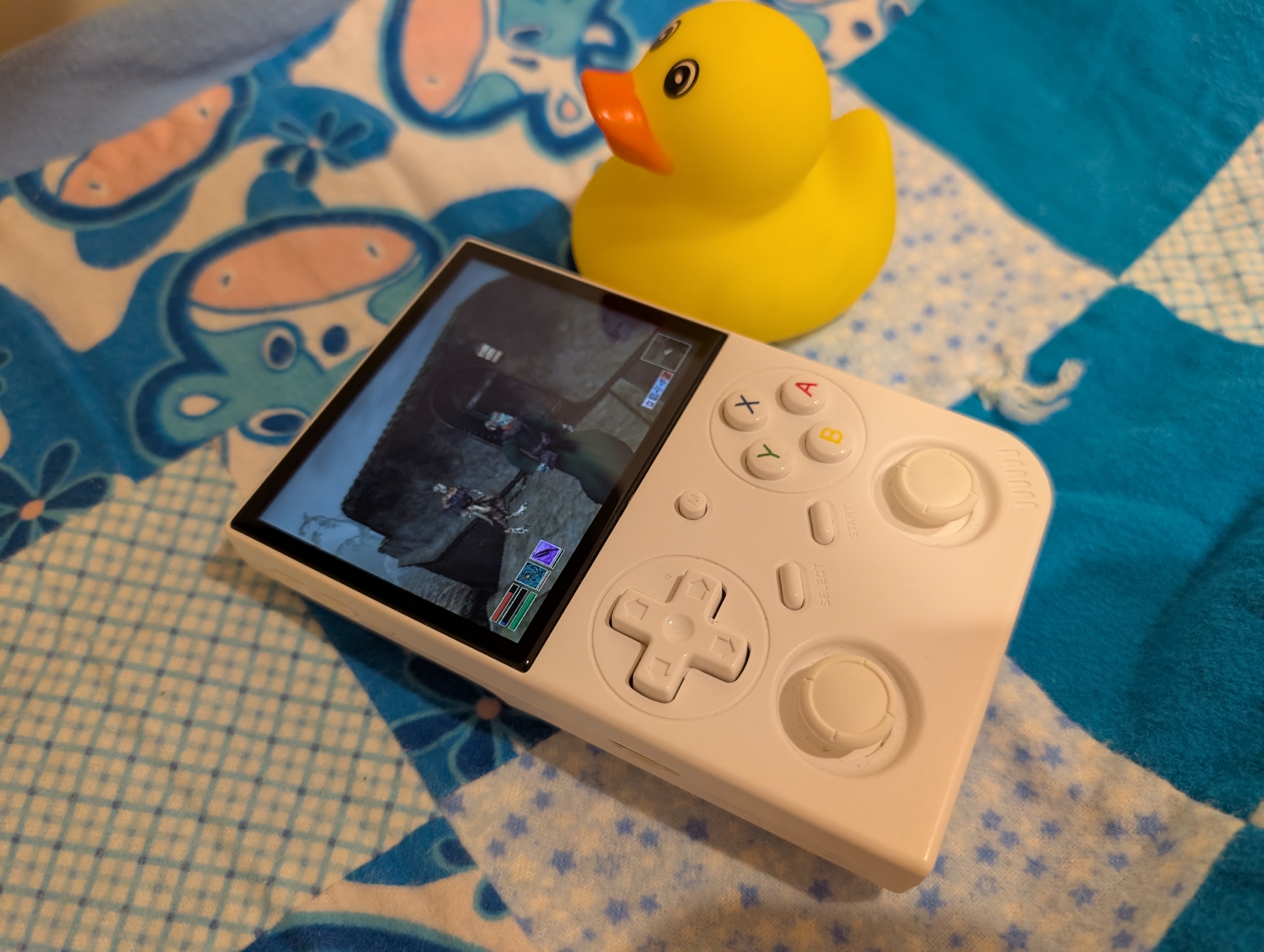 Morrowind running on Anbernic RG35XX Pro - the handheld is on a baby blanket, next to a rubber duck. Photo by author.