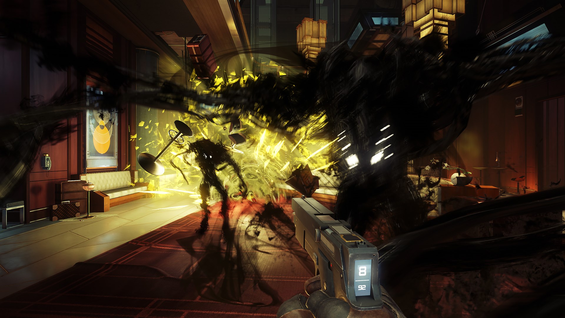 A screenshot from Prey shows a first-person view of a character holding a weapon and facing a shadowy, alien creature amidst an explosion of yellow light in a room.