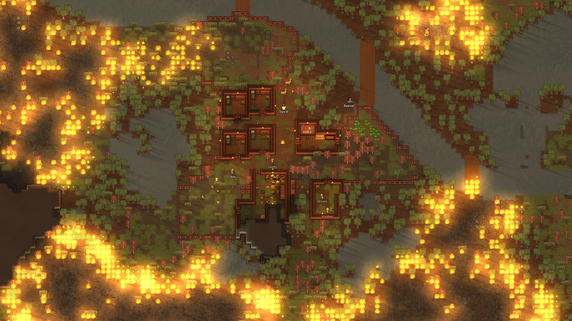 In RimWorld, a wooden colony base is surrounded by encroaching wildfires spreading through the trees and grass. Image courtesy of Ludeon Studios.