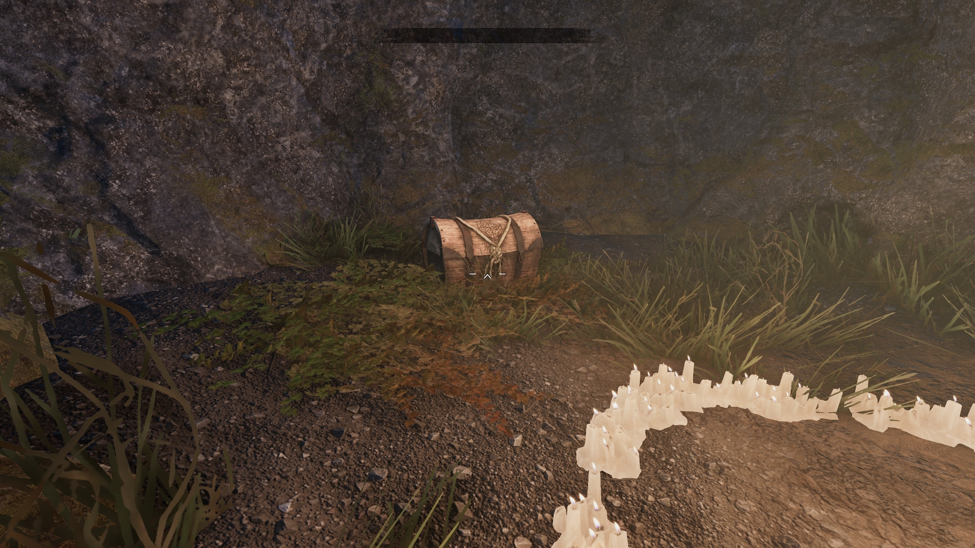 A wooden chest with rope and Celtic knot details sits near candles and mossy rocks in Tainted Grail. Screenshot by author.