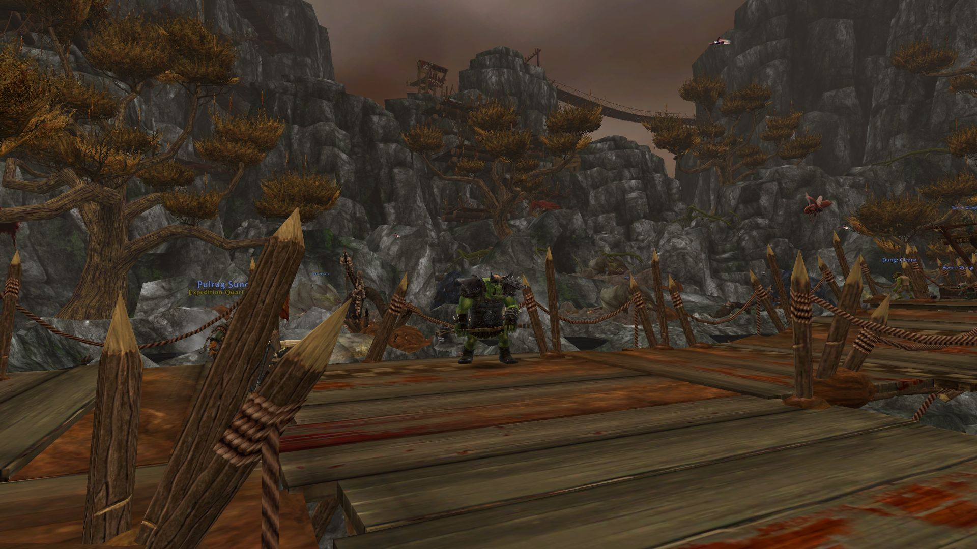 Warhammer Online: Return of Reckoning shows an orc character on a spiked wooden bridge leading to a mountainous fort under a red sky.